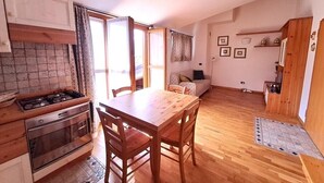 A compact kitchen with a wooden table and chairs, a stove, and a sink. There is a sofa and a small dining table in the living area. - Bright one-bedroom apartment with panoramic view terrace (Chiesa In Valmalenco)