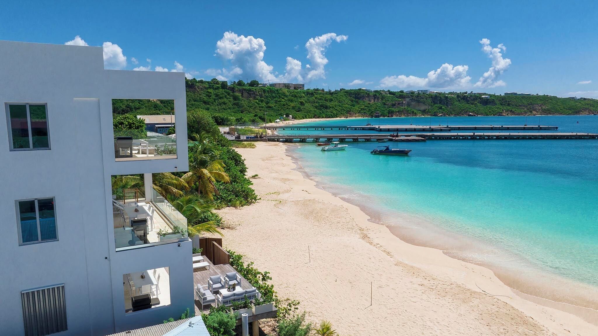 Un edificio moderno con numerosi balconi affacciati su una spiaggia e un molo che si estende verso il mare.