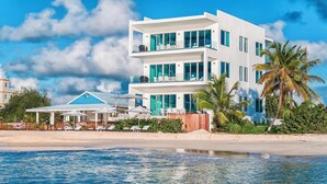A modern multi-story hotel with balconies, a poolside area, and a beach view. - Luxury Beachfront Enclave Unit 1 (Sandy Ground)