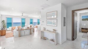 A spacious living area with a large window overlooking the sea, a wooden bench, and a white console table. - Luxury Beachfront Enclave Unit 1 (Sandy Ground)