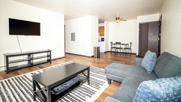 Een moderne woonkamer met een bank, een salontafel, een televisie en een eethoek in de achtergrond.
