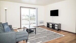 Een moderne woonkamer met een bank, een salontafel, een flatscreen-televisie, een tv-meubel en een grote schuifpui naar een balkon.
