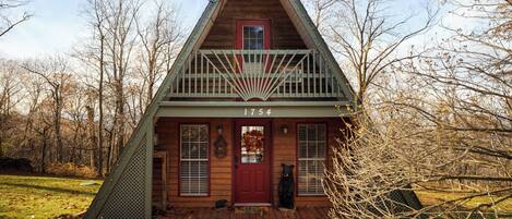 A wooden cabin with a red door, a balcony, and the number 1754 on the front.