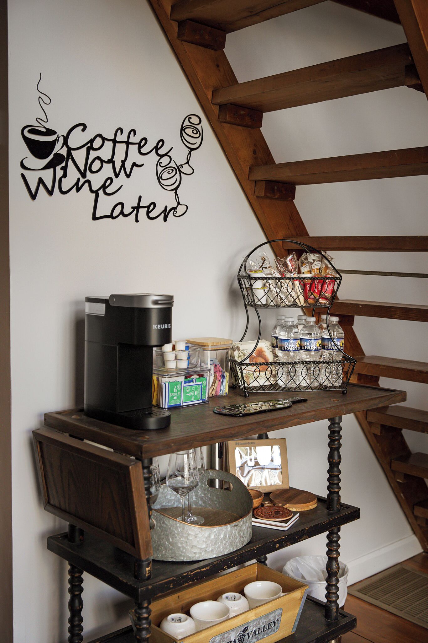 Eine Kaffeestation mit einer Keurig-Kaffeemaschine, einem Weinkühler und einem Weinglas auf einer Holzablage.
