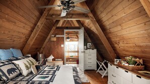 A cozy attic bedroom with a sloped ceiling, a bed with a checkered quilt, a white dresser, and a basket on the dresser.
