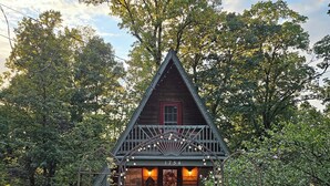 A wooden cabin with a porch, surrounded by trees and a gravel path. - The Grape Escape - A-Frame Cabin  (Linden)