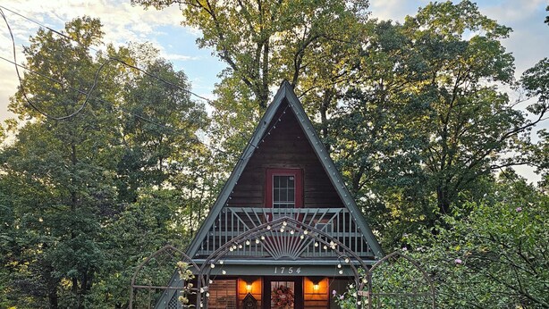 A wooden cabin with a porch, surrounded by trees and a gravel path.