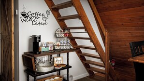 A staircase with wooden railings, a coffee maker, a shelf with glassware, and a wall sign saying "Coffee Now Wine Later".