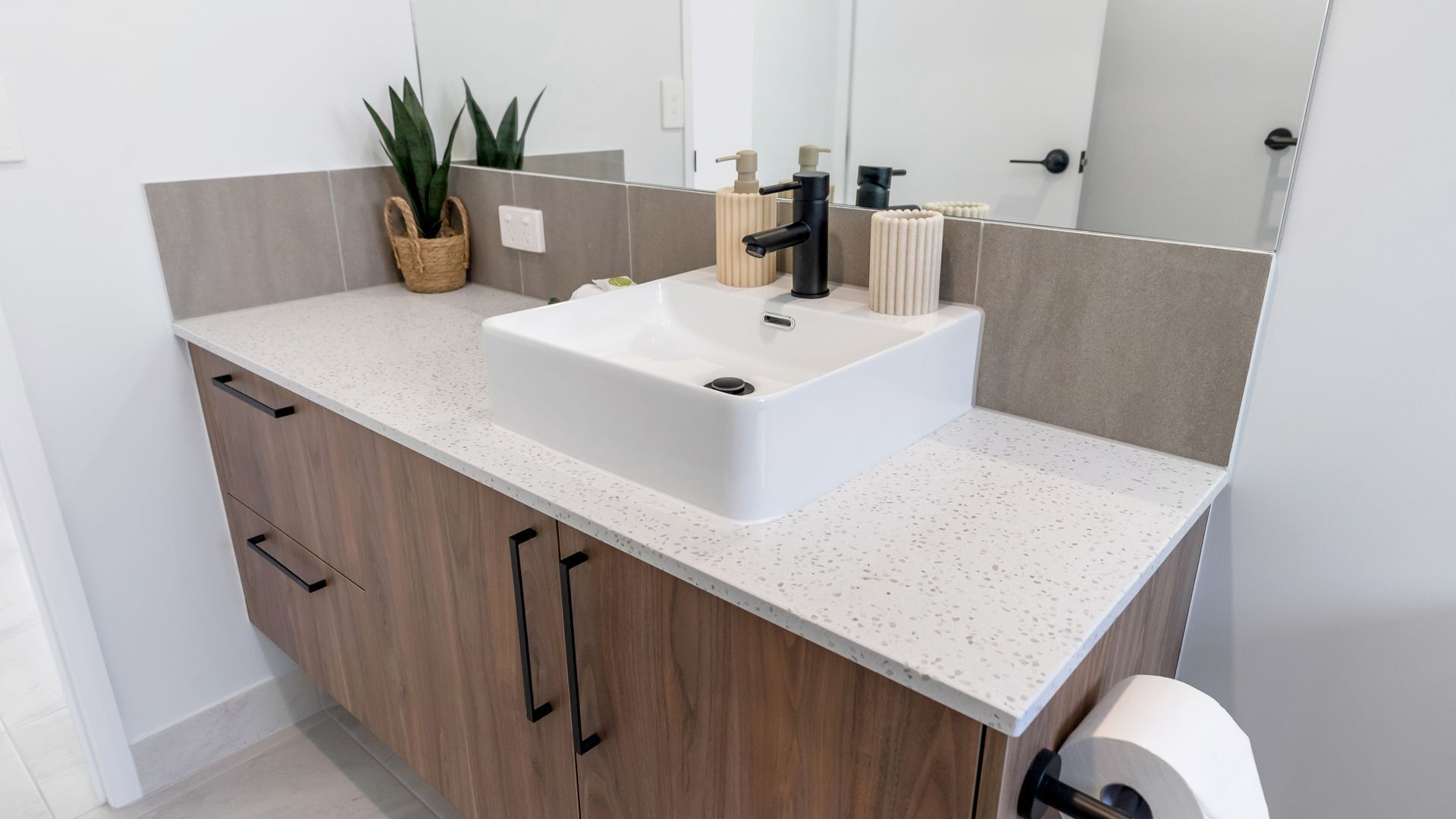 A modern bathroom with a white sink, wooden cabinets, a mirror, and a toilet.