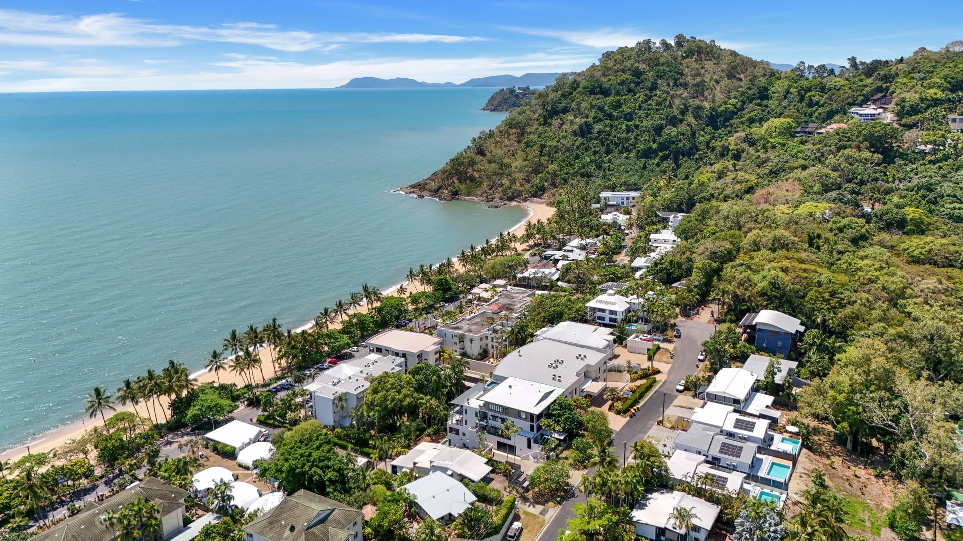 Un quartier résidentiel en bord de mer, avec des maisons modernes, une plage et un paysage vallonné en arrière-plan.