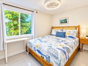 A bedroom with a bed, a bedside table with a lamp, a window with curtains, and a ceiling fan.
