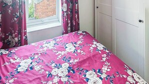 Una camera da letto con una coperta dal disegno floreale, una finestra con tende e una porta bianca.