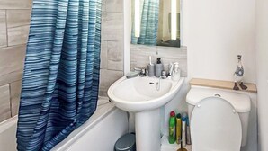 Un bagno con un lavandino bianco, un water, un cestino e una tenda da doccia.