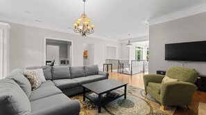 A modern living room with a sectional sofa, a coffee table, a patterned rug, a green armchair, and a flat-screen TV.