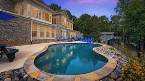 A house with a swimming pool, stone exterior, and blue chairs.