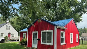 Una casa roja de un piso con techo azul, detalles blancos y el número 650 en la puerta.