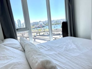 A hotel room with a large window offering a view of a cityscape, including a bridge and a body of water.