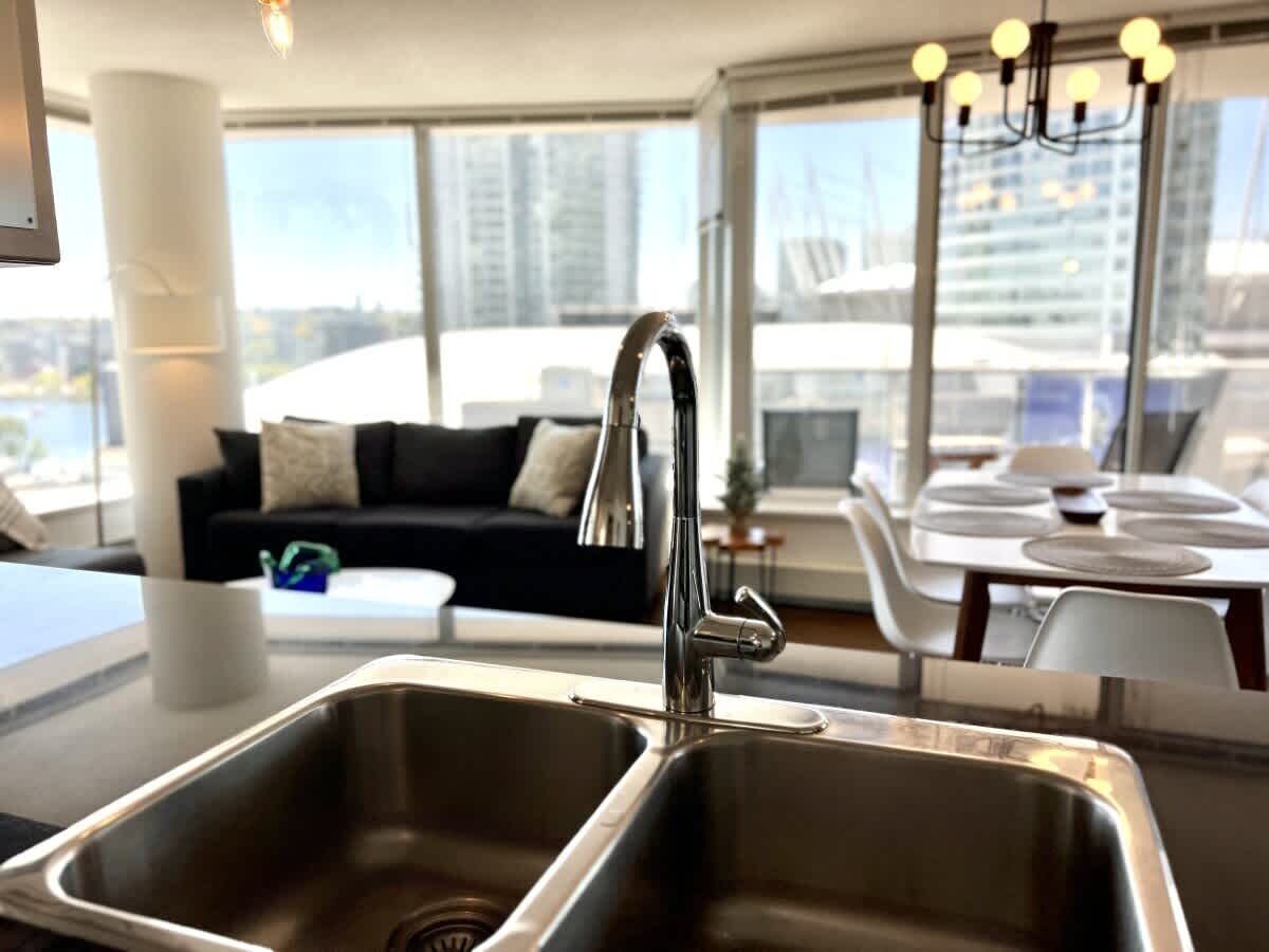 Una cocina moderna con un lavamanos de acero inoxidable, una encimera negra y un comedor con sillas blancas y una mesa.