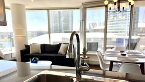 Une cuisine moderne dotée d’un évier en acier inoxydable, d’un plan de travail noir et d’un coin repas avec des chaises et une table blanches.