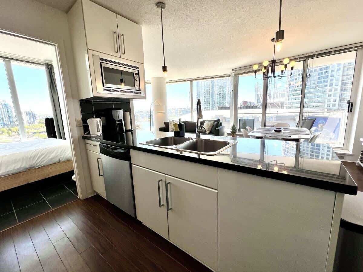 Una cocina moderna con microondas, lavamanos y armarios, una cama con vistas y un amplio ventanal con vista a la ciudad.