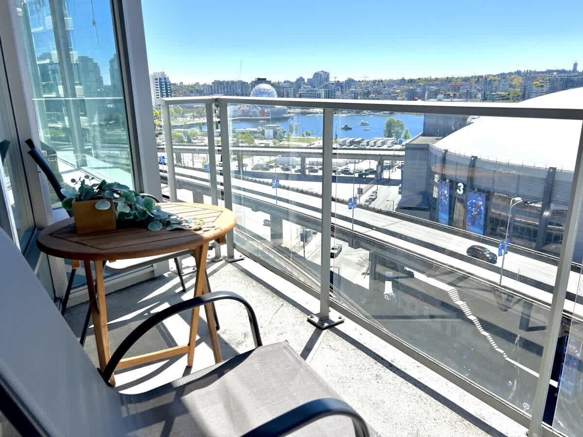 Un balcón con vistas a un paisaje urbano, una mesa con una silla y una planta en maceta.