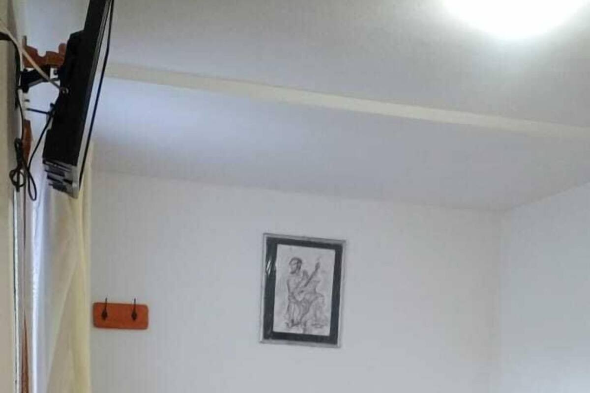 A room with two single beds, a small wooden chair, a framed drawing on the wall, and a television mounted on the wall.