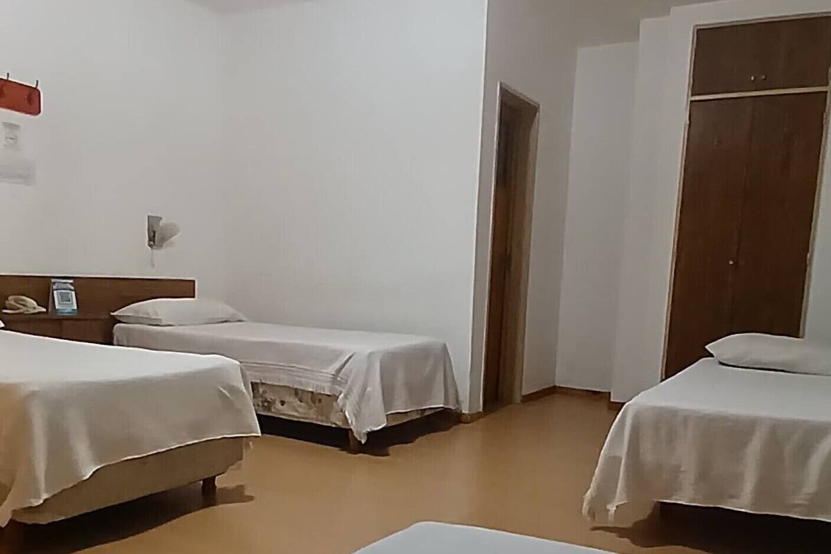 A hotel room with three single beds, a wooden wardrobe, and a small table.