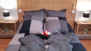 A bed with a wooden headboard, grey and black bedding, and a small vase with flowers. There are two bedside tables with lamps. - Holiday Home 'Au Nid Douillet' with Shared Terrace, Shared Garden and Wi-Fi (Bourges)