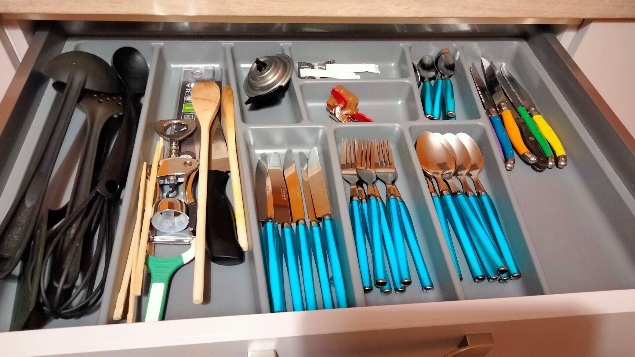 A drawer with various kitchen utensils and tools, including spoons, knives, and a grater.
