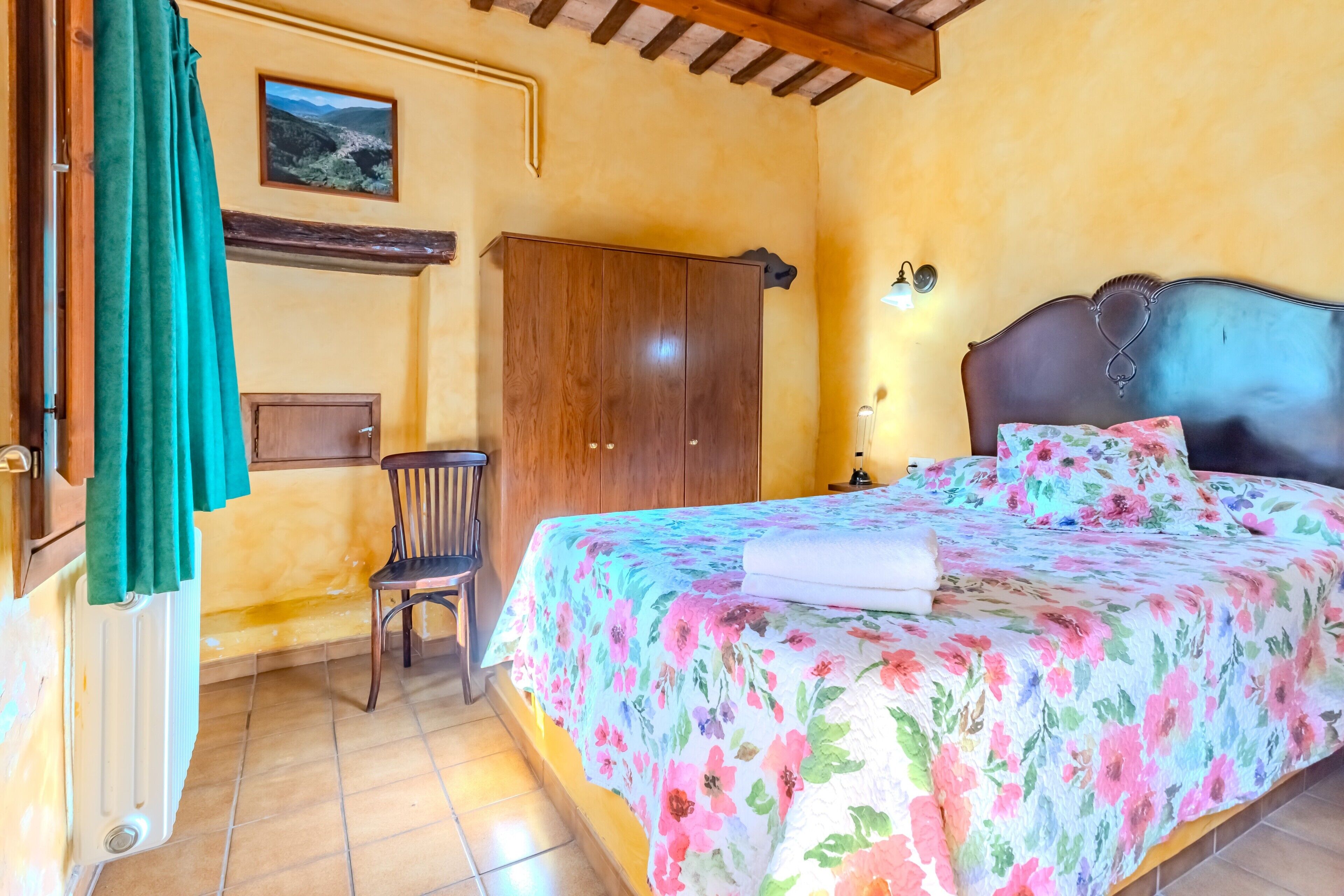 A bedroom with a bed, a wooden wardrobe, a chair, a radiator, and a picture on the wall.