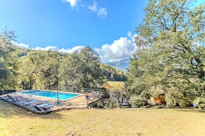 A swimming pool with lounge chairs, surrounded by trees and a small building. - Rural House 'Can Guidic' with Mountain Views, Private Pool and Wi-Fi (La Vall D' en Bas)