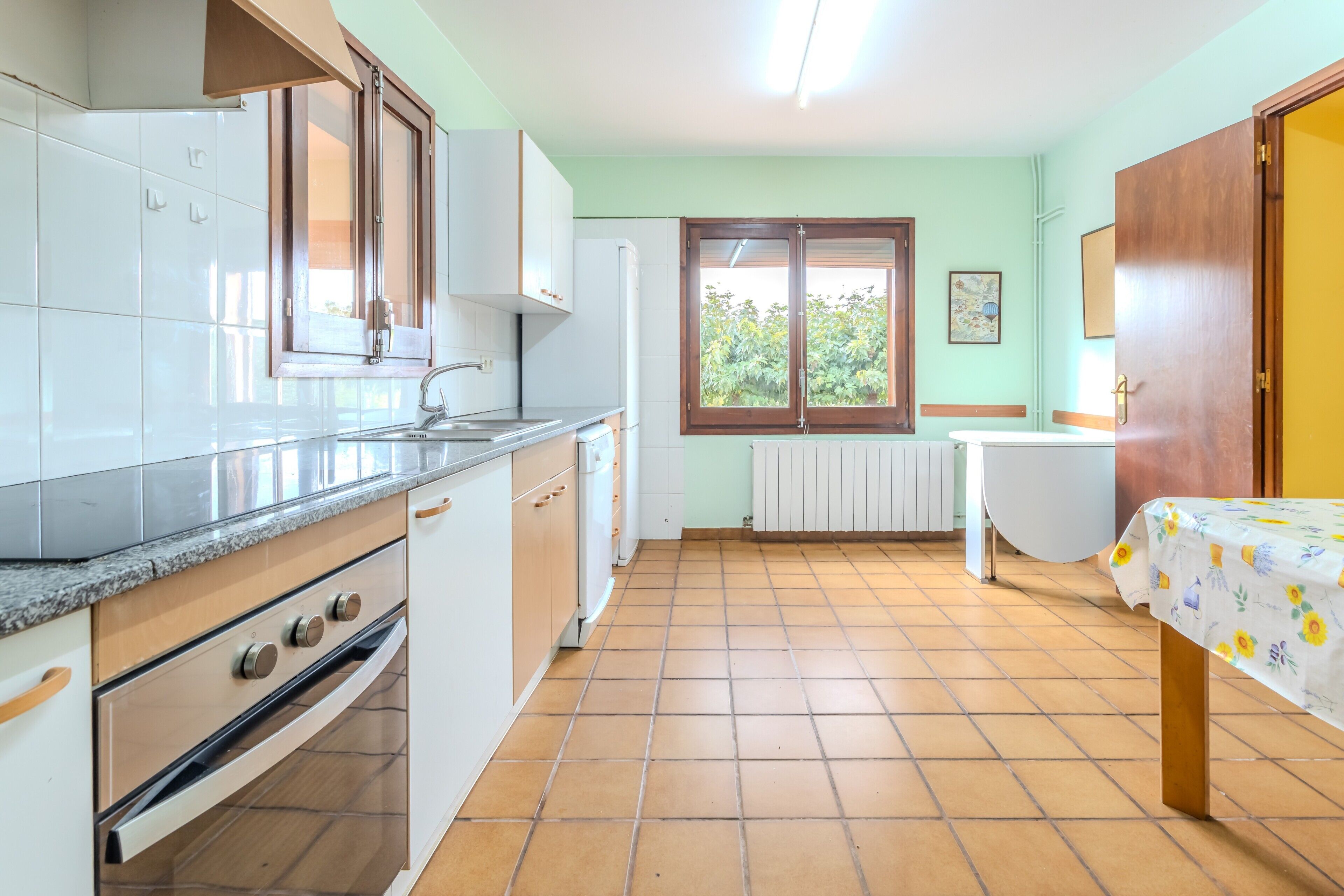 A kitchen with white cabinets, a countertop, a window, and a view of greenery outside.