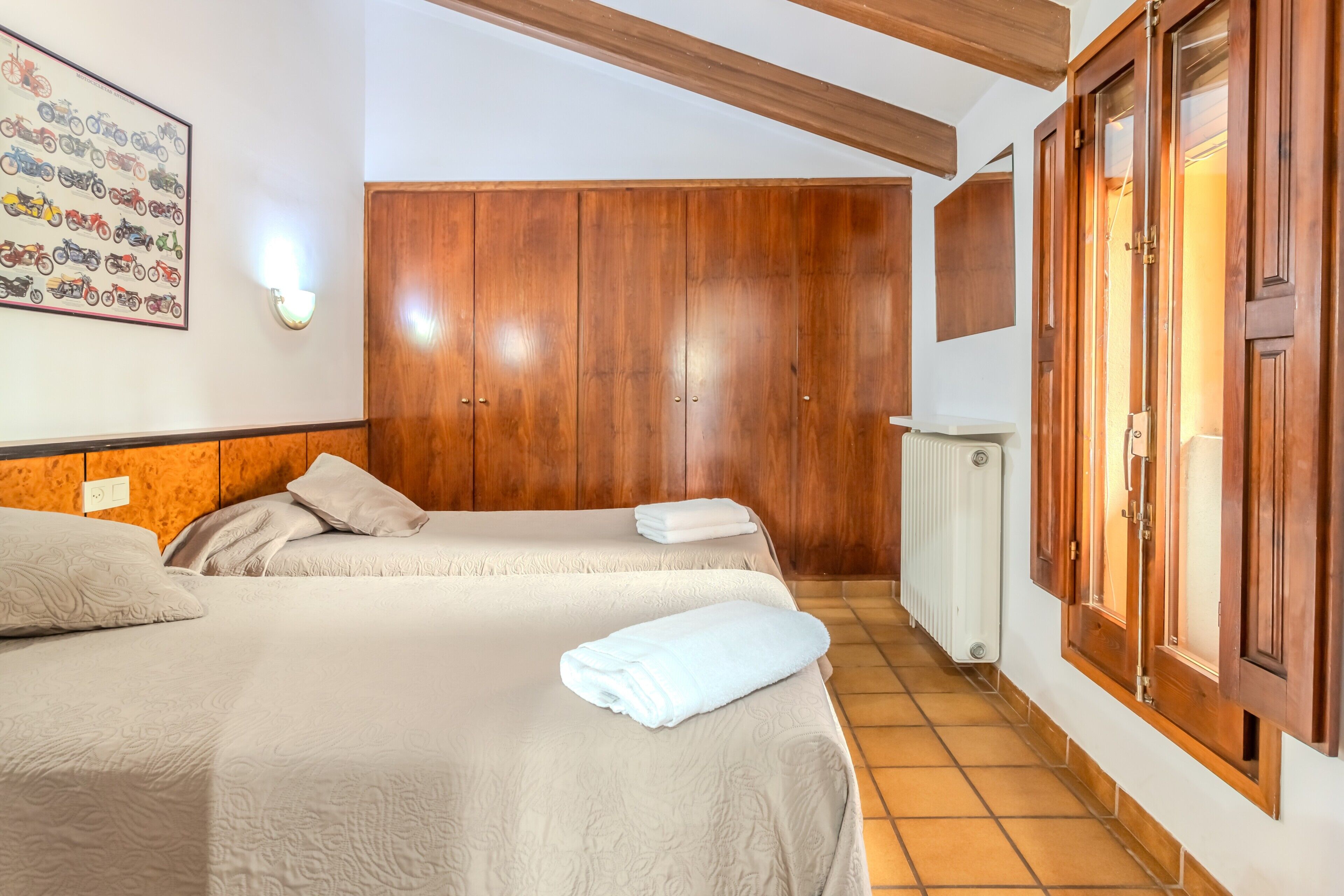 Habitación de hotel con dos camas, un armario de madera, una luz empotrada en la pared y un radiador.