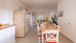 A modern kitchen with white cabinetry, a wooden dining table, and a refrigerator. - Villa 'La Collina' with Private Terrace, Wi-Fi and Air Conditioning (Galatone)