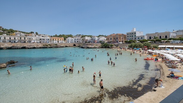 A beach with people swimming and sunbathing, a rocky shoreline, and buildings in the background. - Villa 'La Collina' with Private Terrace, Wi-Fi and Air Conditioning (Galatone)