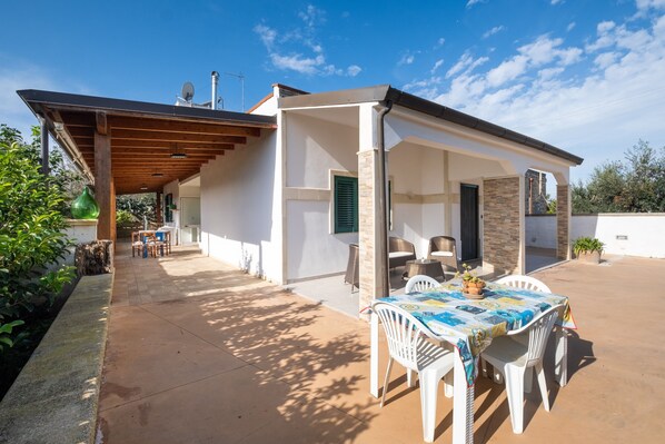 Un patio techado al aire libre con una mesa y sillas, un pérgola y vistas a un edificio.