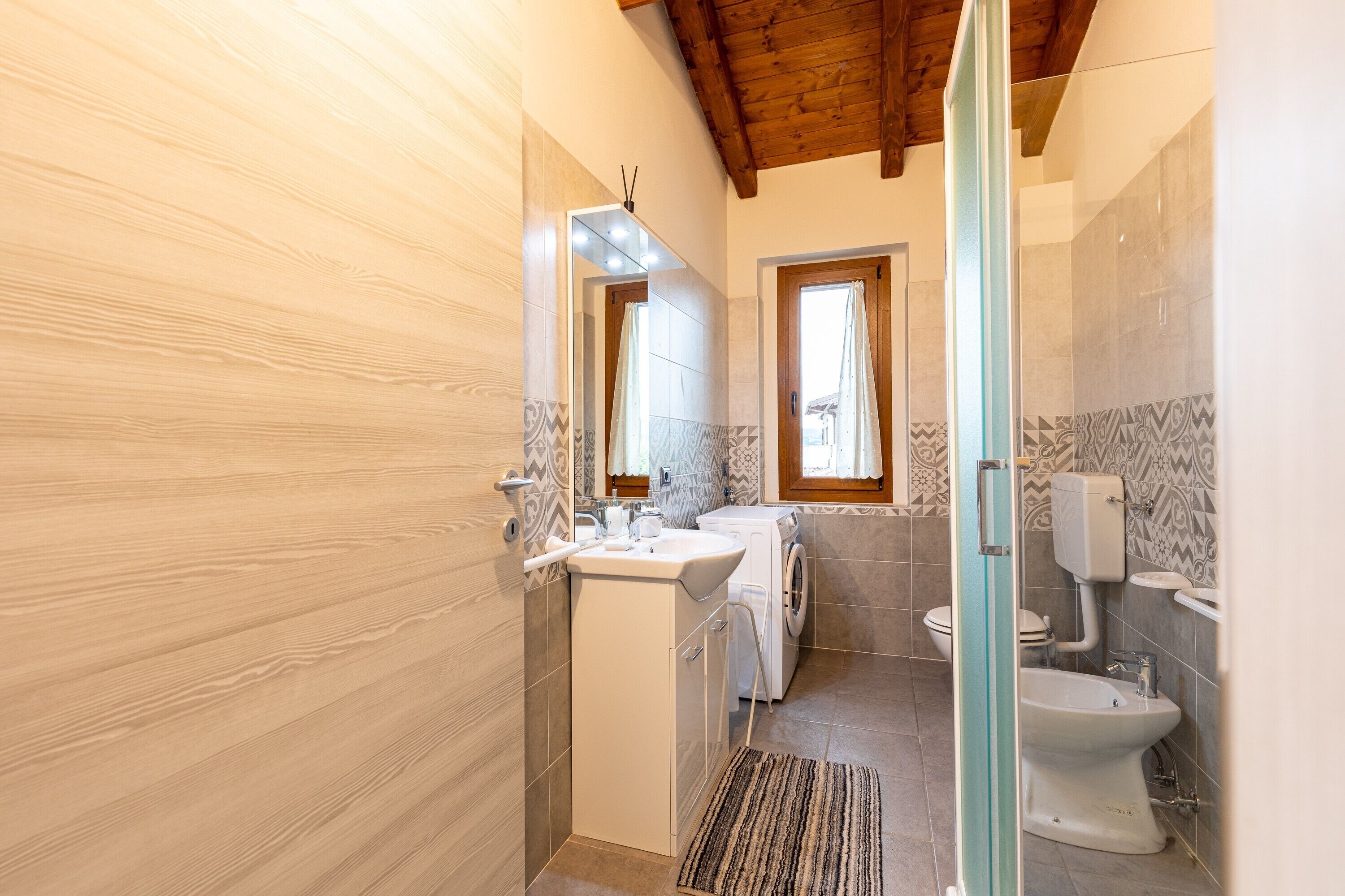 A bathroom with a wooden ceiling, a sink, a washing machine, and a toilet.