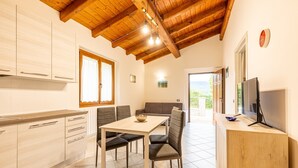 A modern kitchen with wooden beams, a dining area with a table and chairs, and a TV on the right. - Holiday Home 'Numero 1' with Shared Garden (Firenzuola)