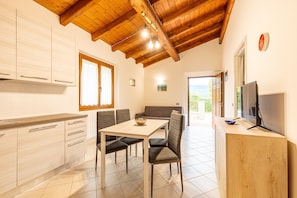 A modern kitchen with wooden beams, a dining area with a table and chairs, and a TV on the right.
