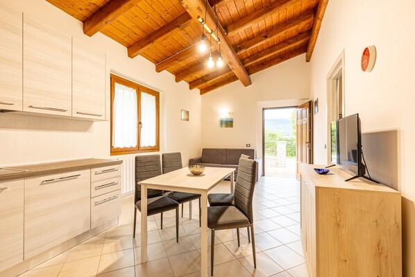 A modern kitchen with wooden beams, a dining area with a table and chairs, and a TV on the right.