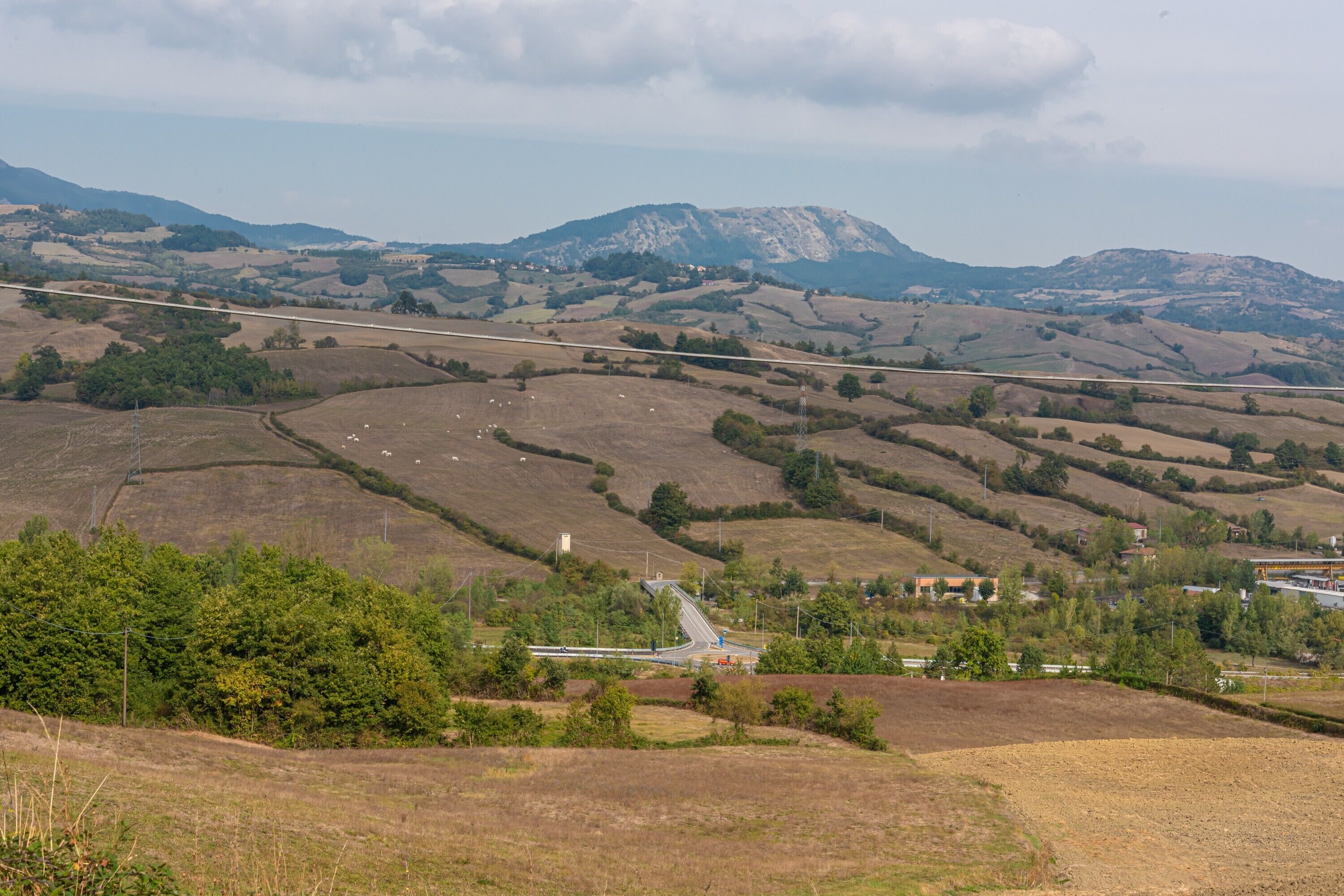 A rural landscape with rolling hills, a road, and a small settlement with buildings.