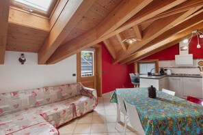 A cozy room with a wooden ceiling, a sofa, a dining table, and a kitchen area.