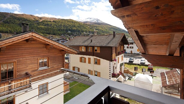 Un edificio de madera con balcones, una montaña al fondo y un cielo despejado.