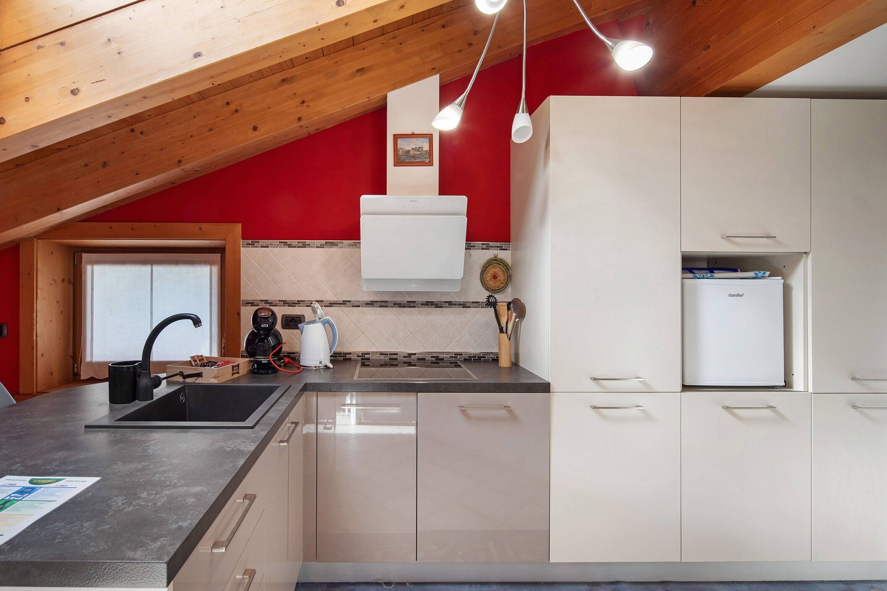 A kitchen with a wooden ceiling, a sink, a kettle, and a refrigerator.