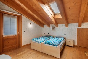 Una habitación con techo de madera, tragaluz, cama con ropa de cama a cuadros, mesita de noche y armario.
