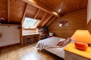 A wooden cabin bedroom with a lofted desk, a bed with pillows, and a lamp on a wooden nightstand. - Apartment "Locdecharme" with Mountain Views, Private Terrace, and Wi-Fi (Les Clefs)