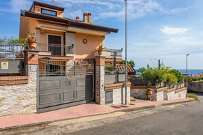 Une maison à deux étages avec une entrée sécurisée par un portail, un balcon et une vue sur la mer.