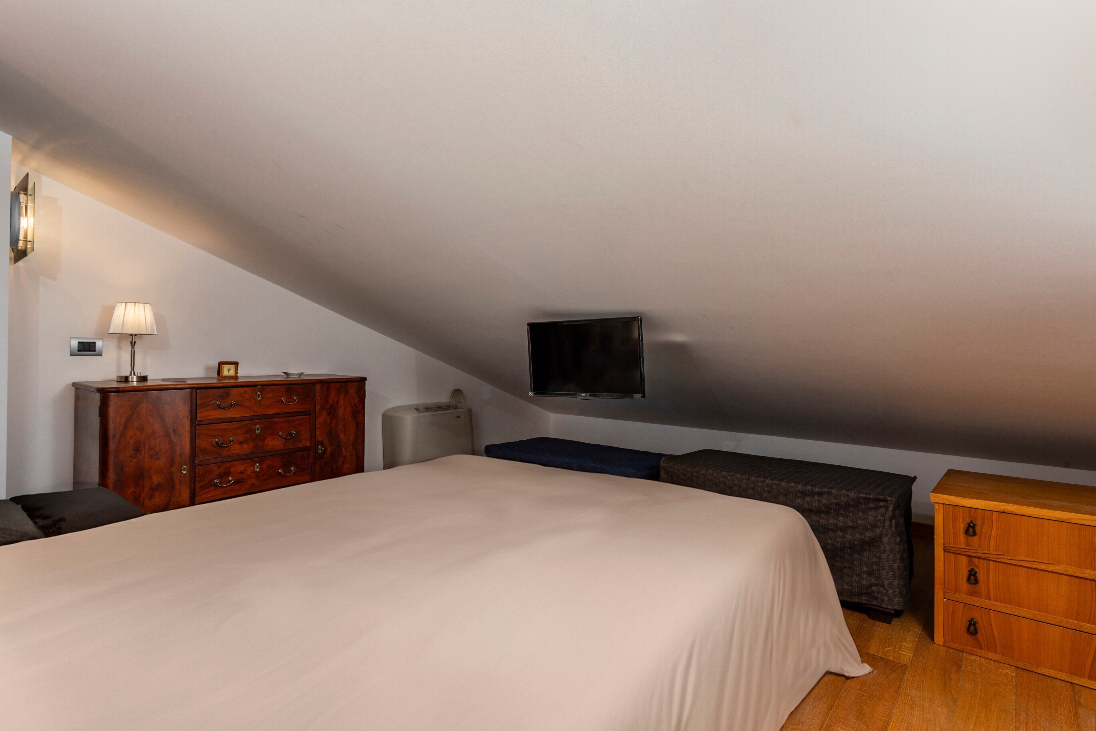Une chambre à coucher avec un lit, une commode, une télévision et un banc.