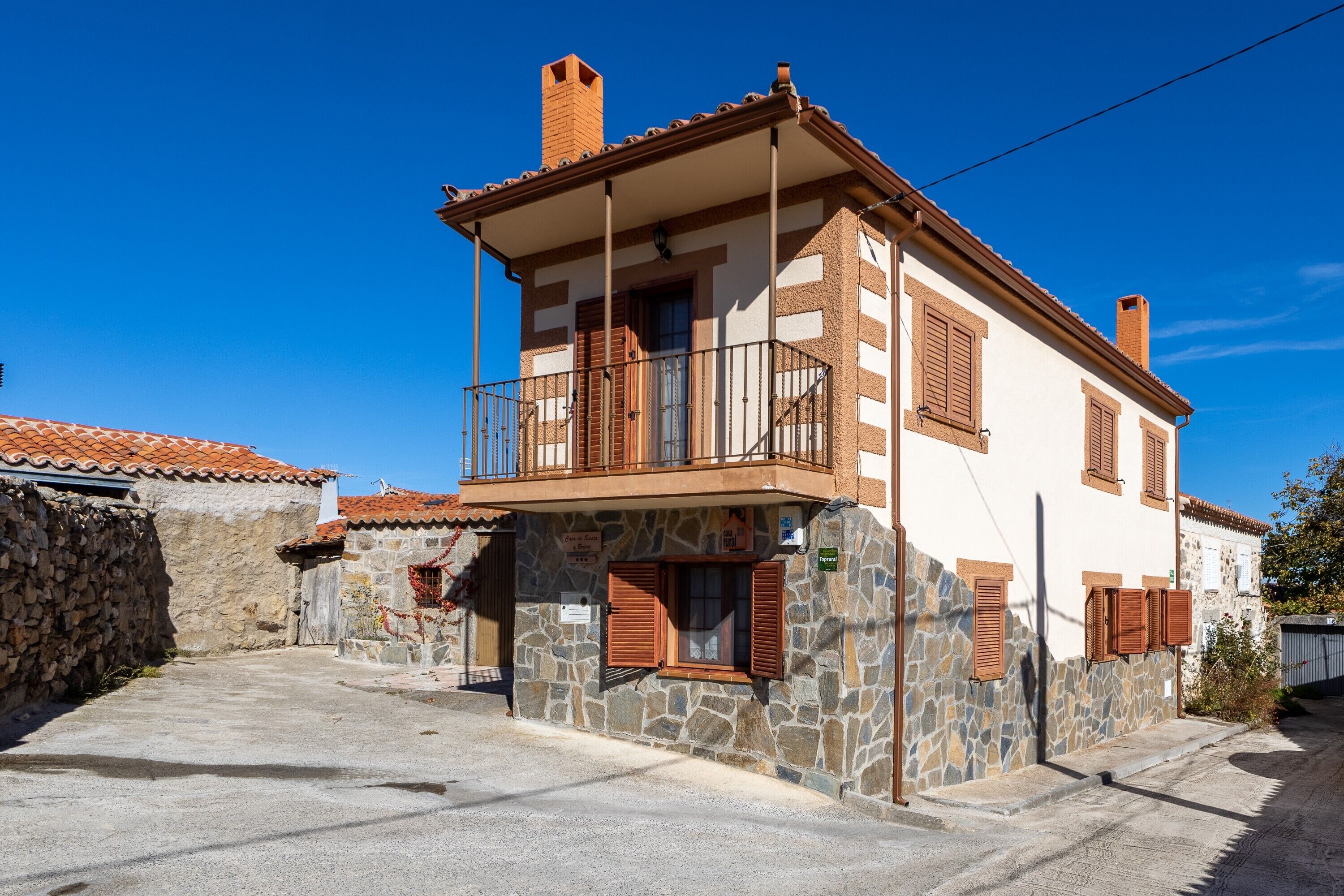 A two-story stone building with a balcony, a stone wall, and a tiled roof.