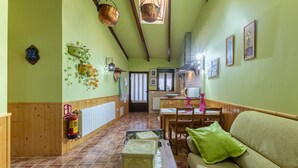Un couloir avec un plancher en bois, un canapé vert, une table à manger et un extincteur.